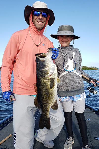 Bass fishing guide and child on a bass fishing boat holding a largemouth bass on Headwaters Lake and Stick Marsh near Vero Beach, FL 